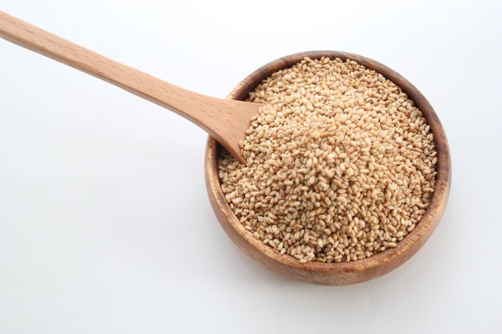 Bowl of white sesame seeds with a wooden spoon