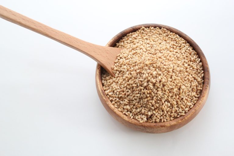 Bowl of white sesame seeds with a wooden spoon
